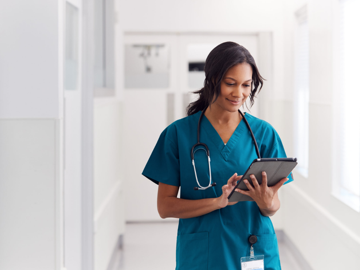 A genderqueer person sitting in a hospital gown sitting in an exam room